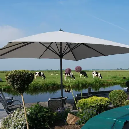 Großer Sonnenschirm auf Terrasse mit Blick auf Weidekühe und ländliche Gartenlandschaft.